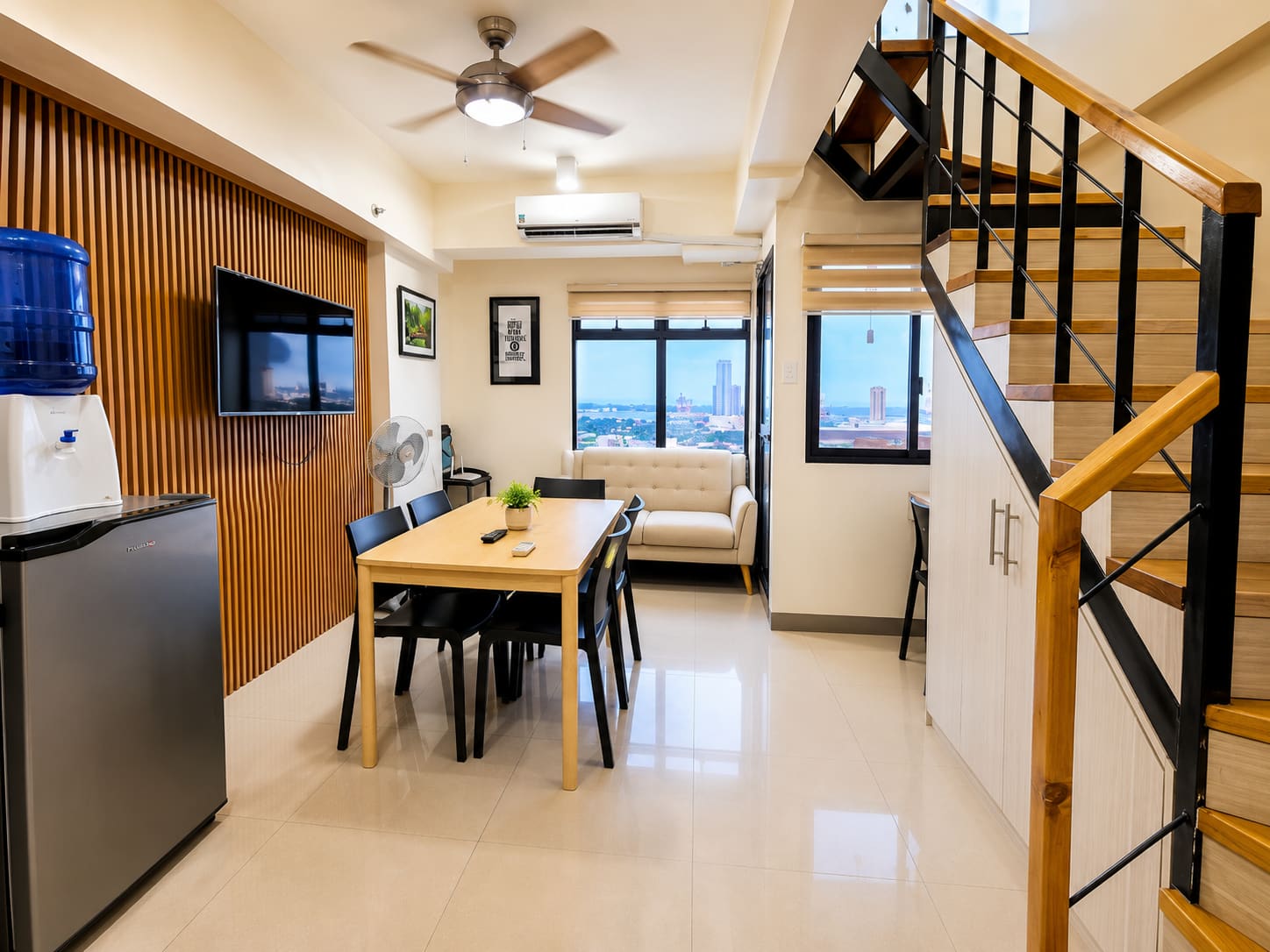 Open dining area with a table for six beside the wooden staircase and windows facing the harbor